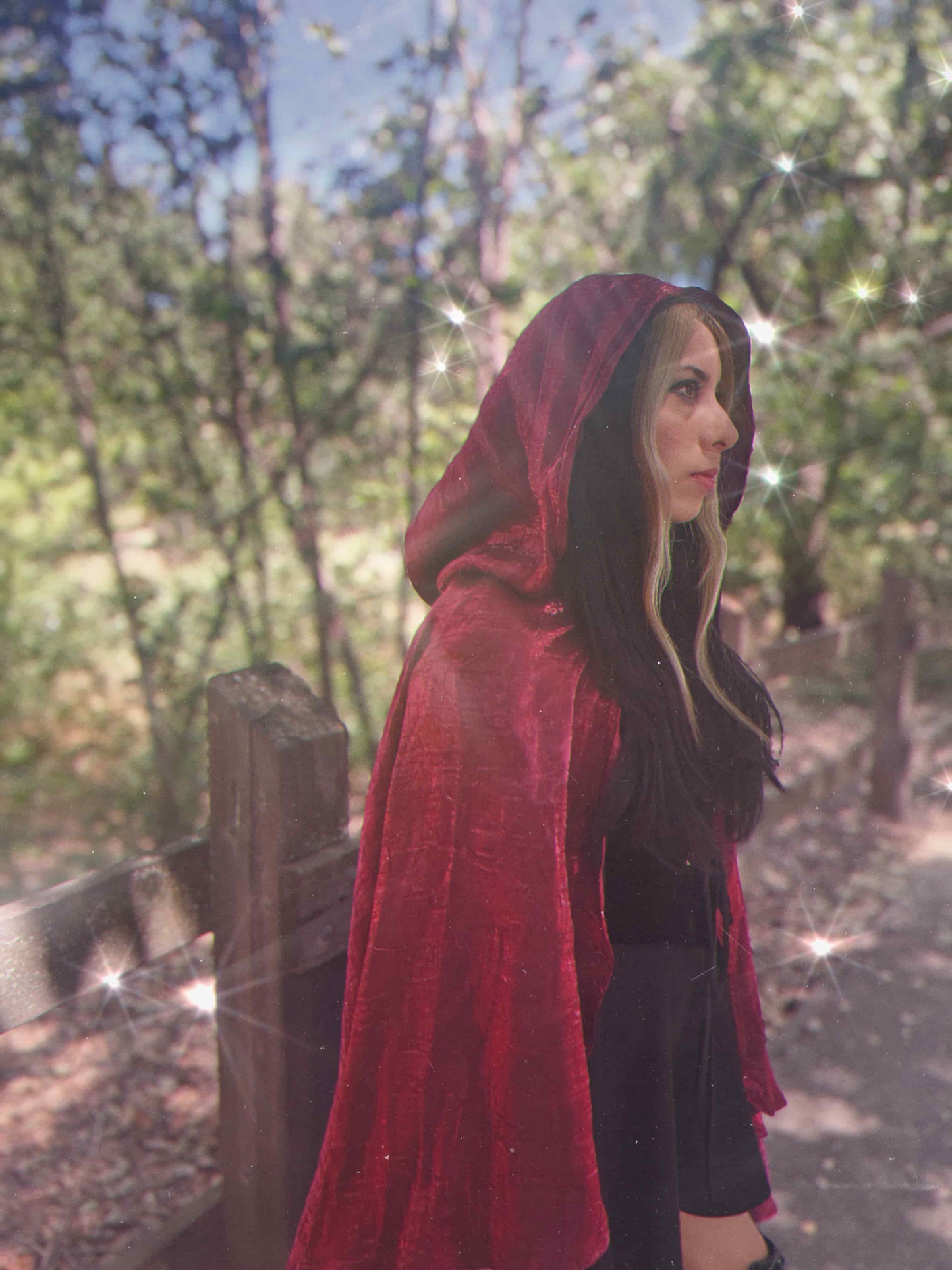Person wearing a red hooded cloak in a forest setting