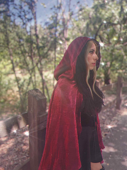 Person wearing a red hooded cloak in a forest setting