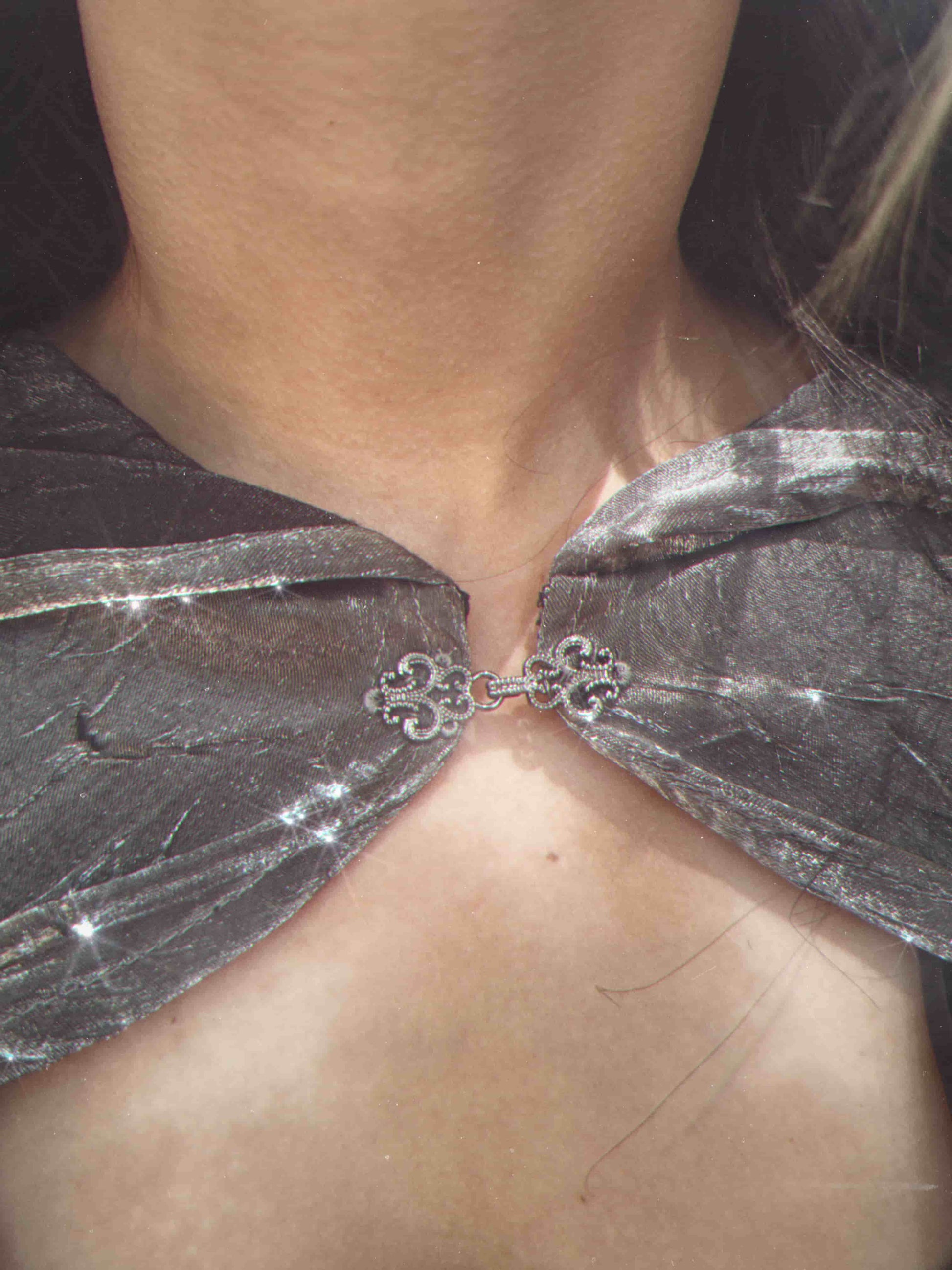 Close-up of a silver cape with decorative clasp on a person.