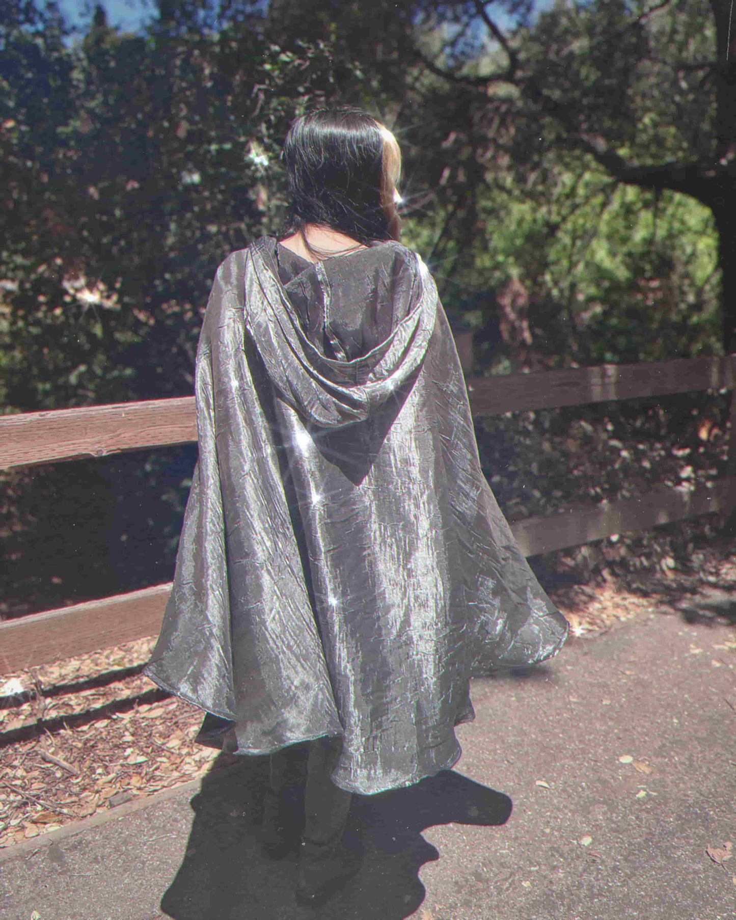 Person wearing a silver cape walking outdoors with trees in the background