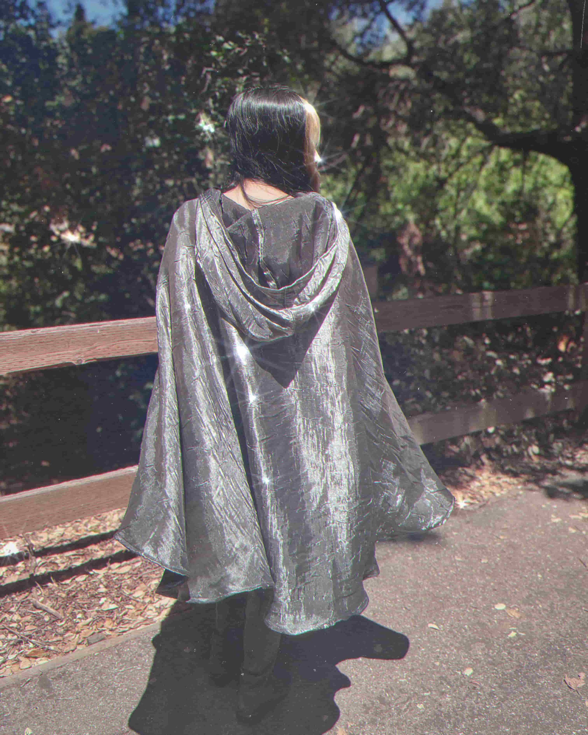 Person wearing a silver cape walking outdoors with trees in the background