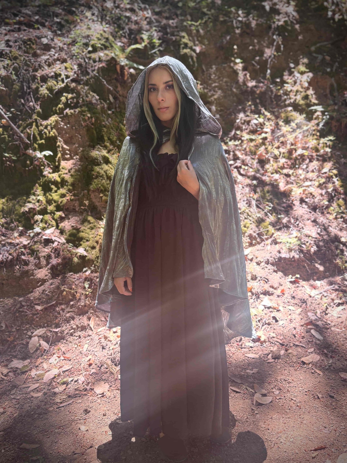 Person wearing a short tiered silver hooded cloak in a forest setting