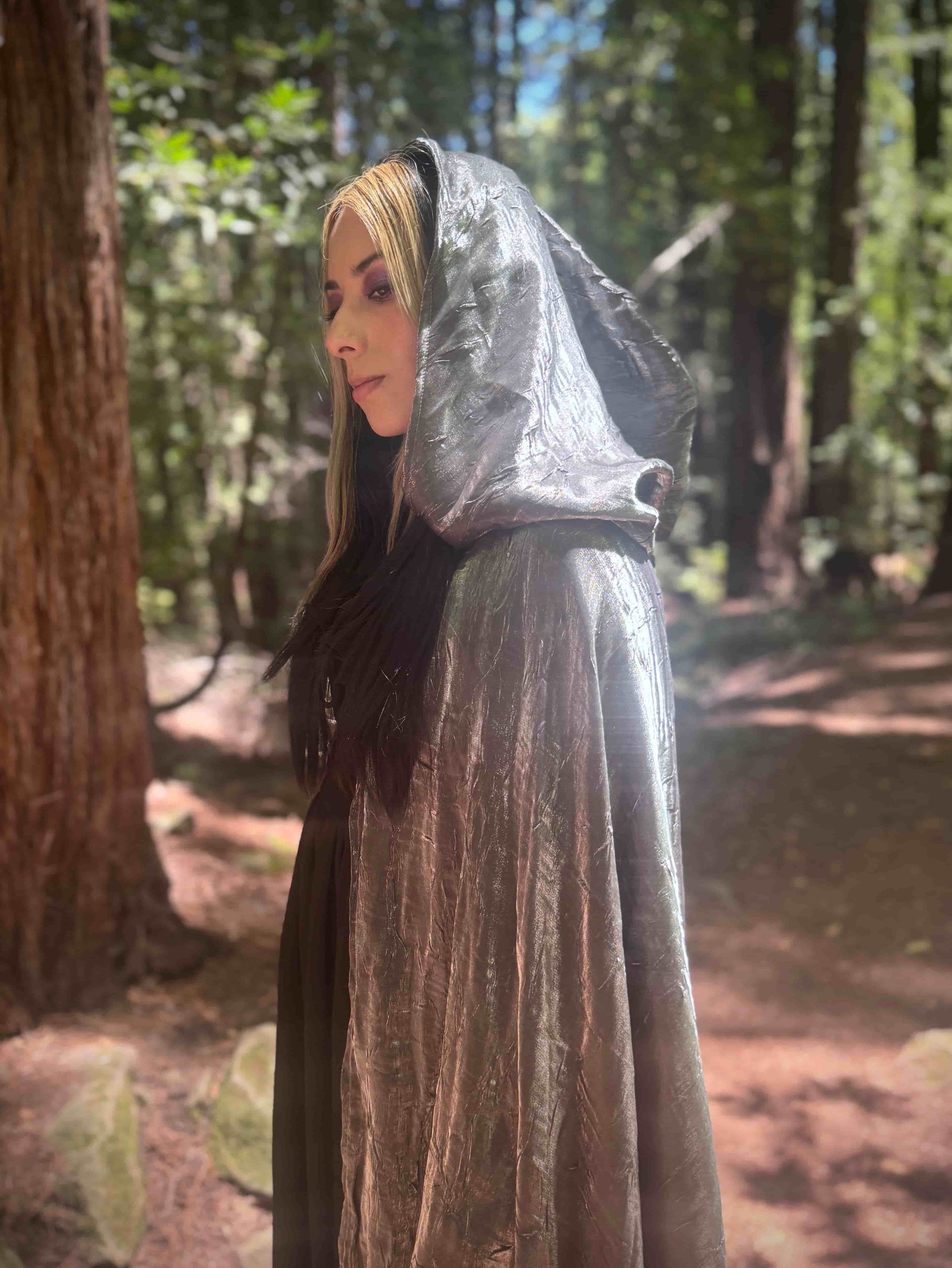 Person wearing a silver hooded cloak in a forest setting