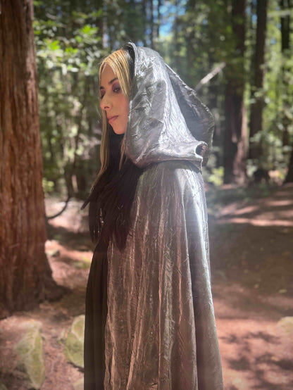 Person wearing a silver hooded cloak in a forest setting
