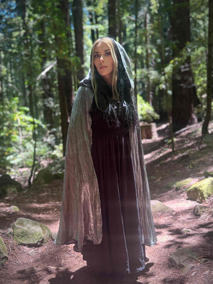 Person wearing a long silver hooded cloak in a forest setting