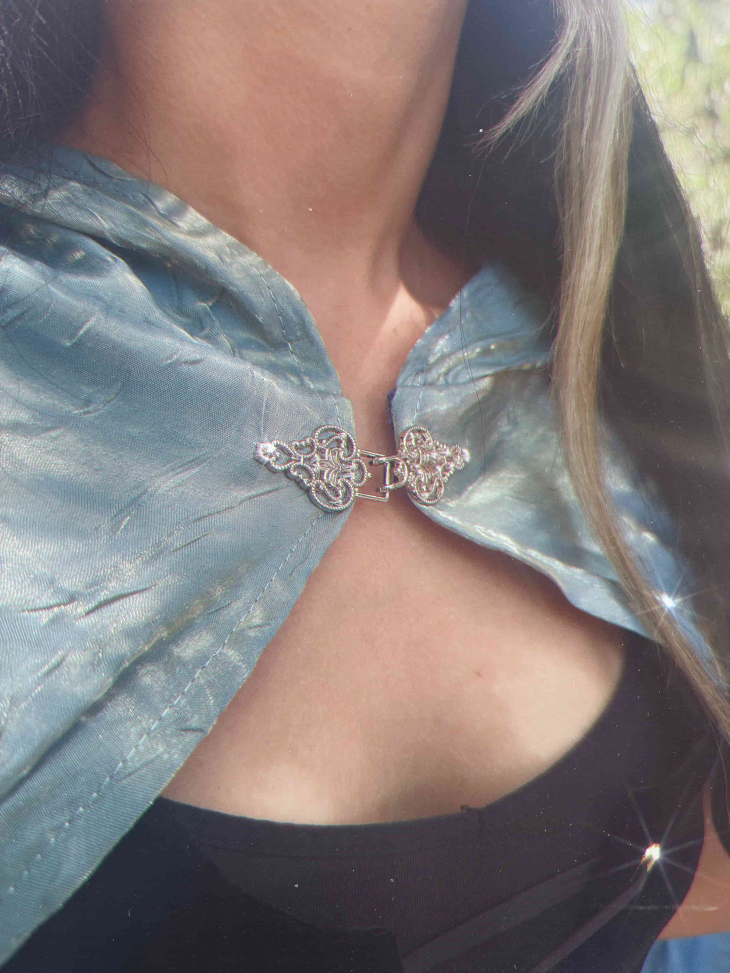 Close-up of a silver ornate clasp on a person wearing a light blue cape.