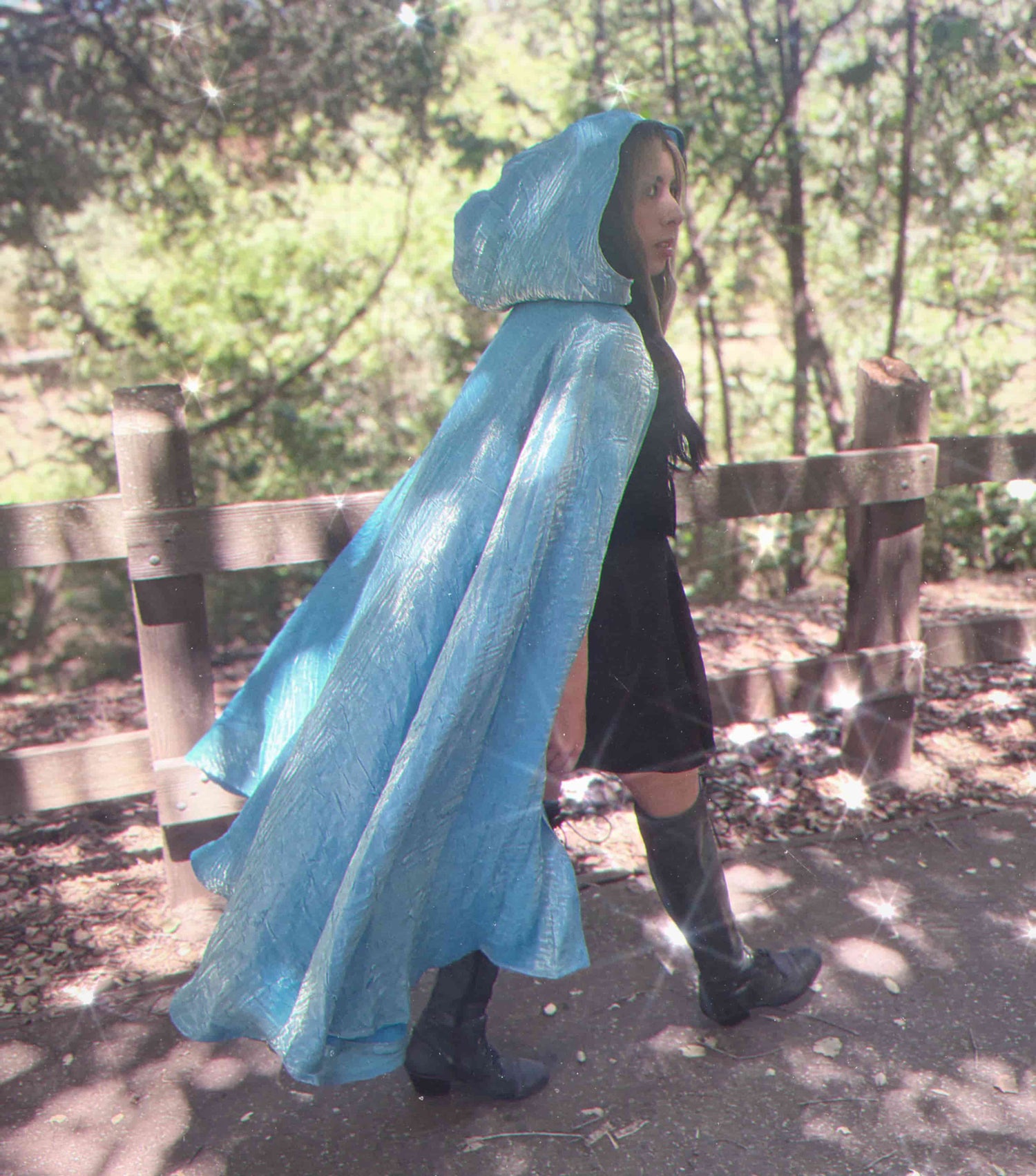 Person wearing a light blue hooded cloak  while walking in a forest setting