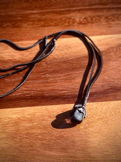 Smoky dark quartz stone pendant wrapped in a black leather cord against a wooden surface