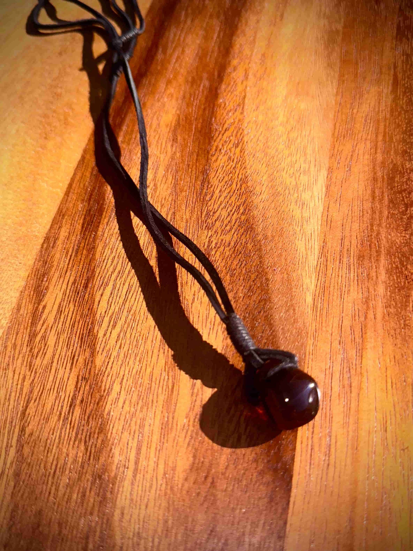 Dark brown pendant on a black cord against a wooden background
