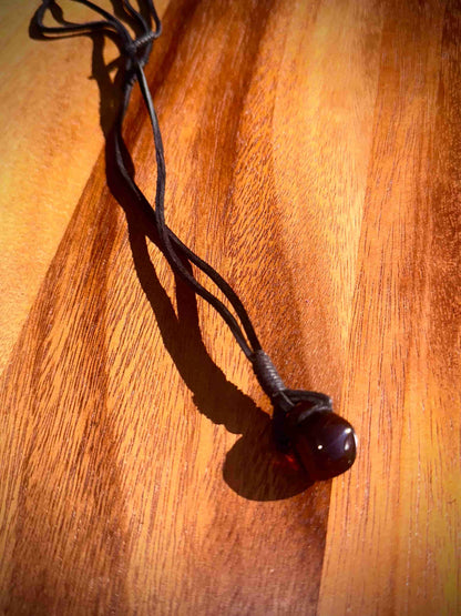 Dark brown pendant on a black cord against a wooden background