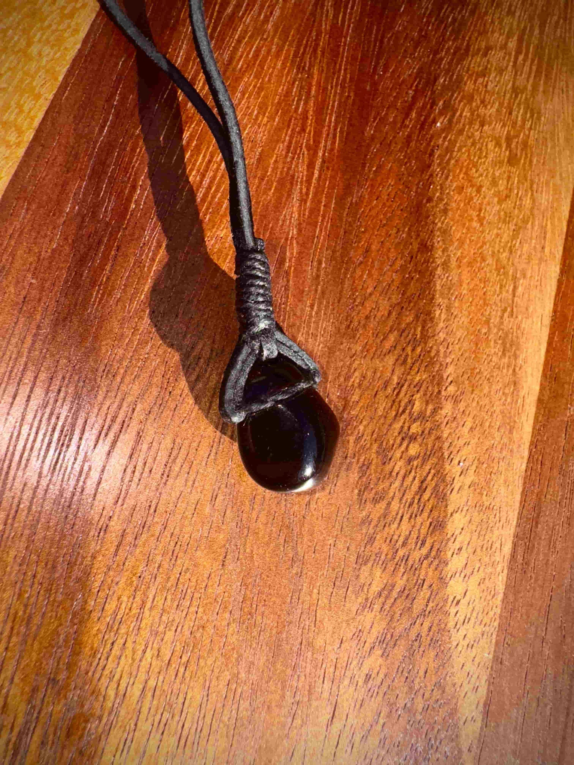 Smoky dark quartz stone pendant on a cord against a wooden surface