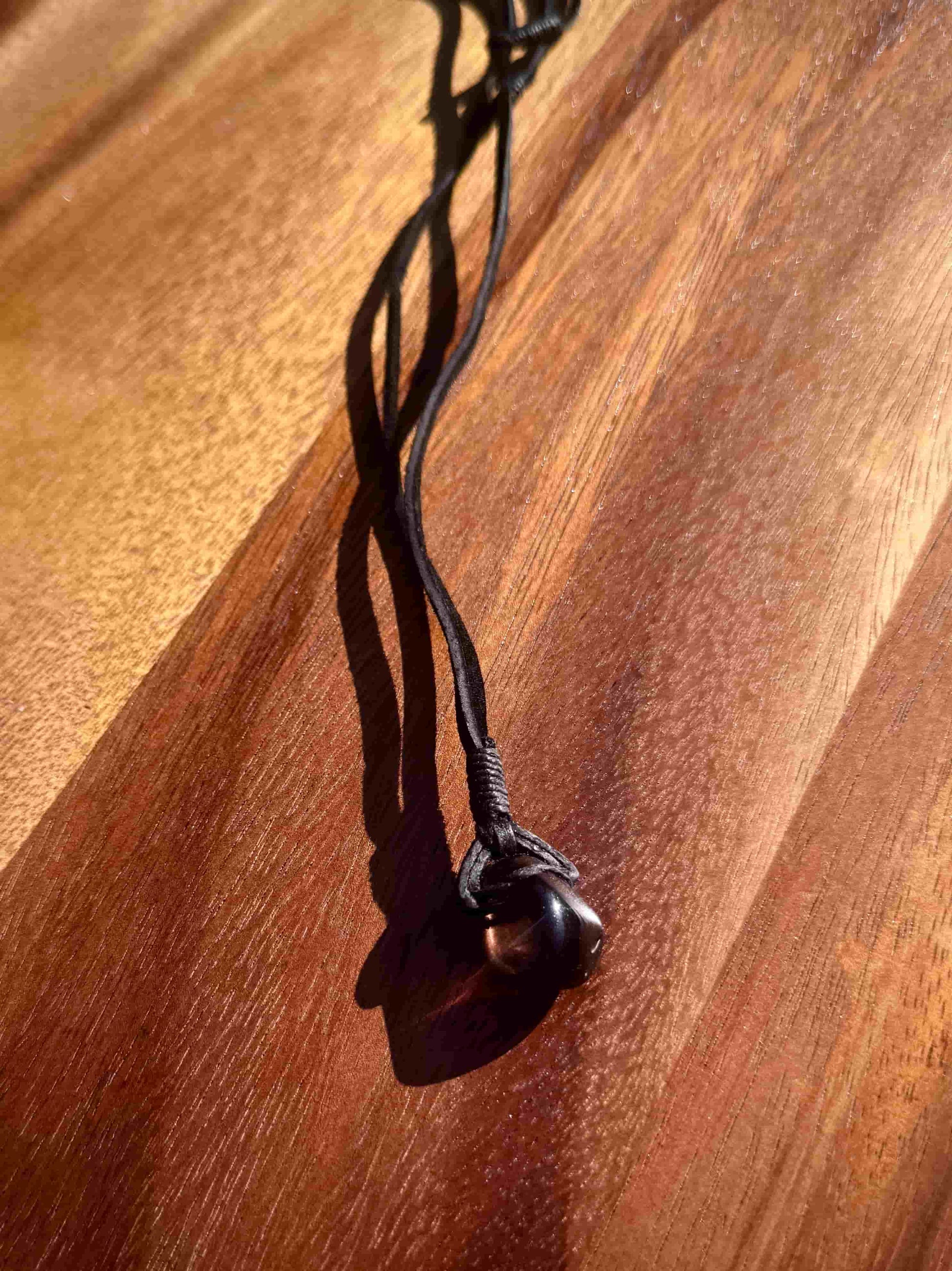 Smoky dark quartz stone pendant wrapped in a black leather cord against a wooden surface
