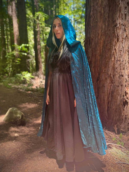 Person wearing a blue hooded cloak in a forest setting