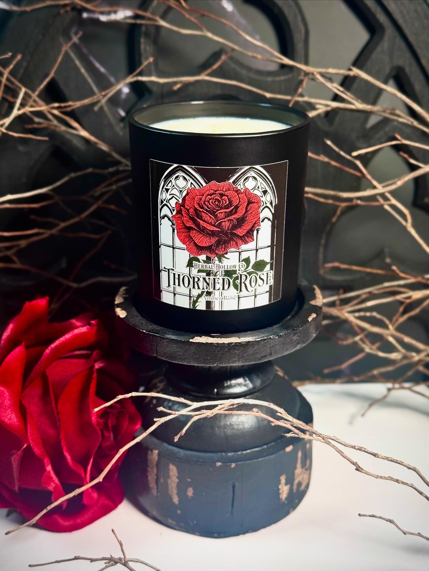 Candle with a red rose design labeled 'Thorned Rose' on a black base with red flowers and branches.