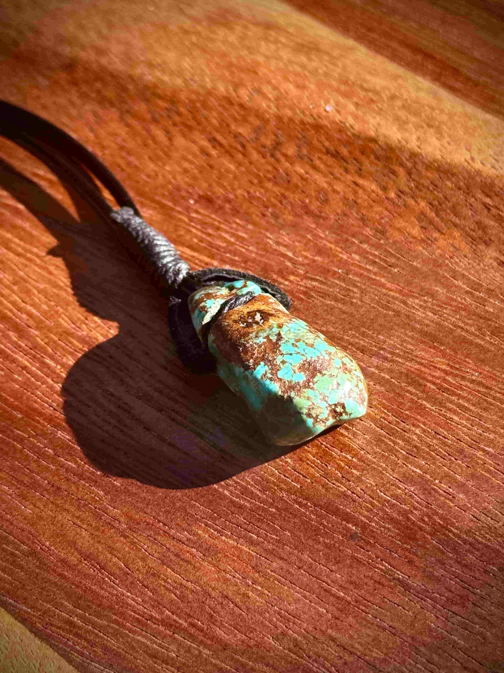 Turquoise stone pendant on a leather cord against a wooden background
