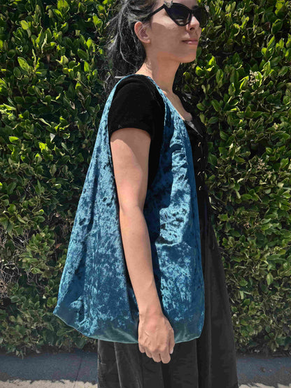 Person wearing a blue velvet bag against a green hedge background