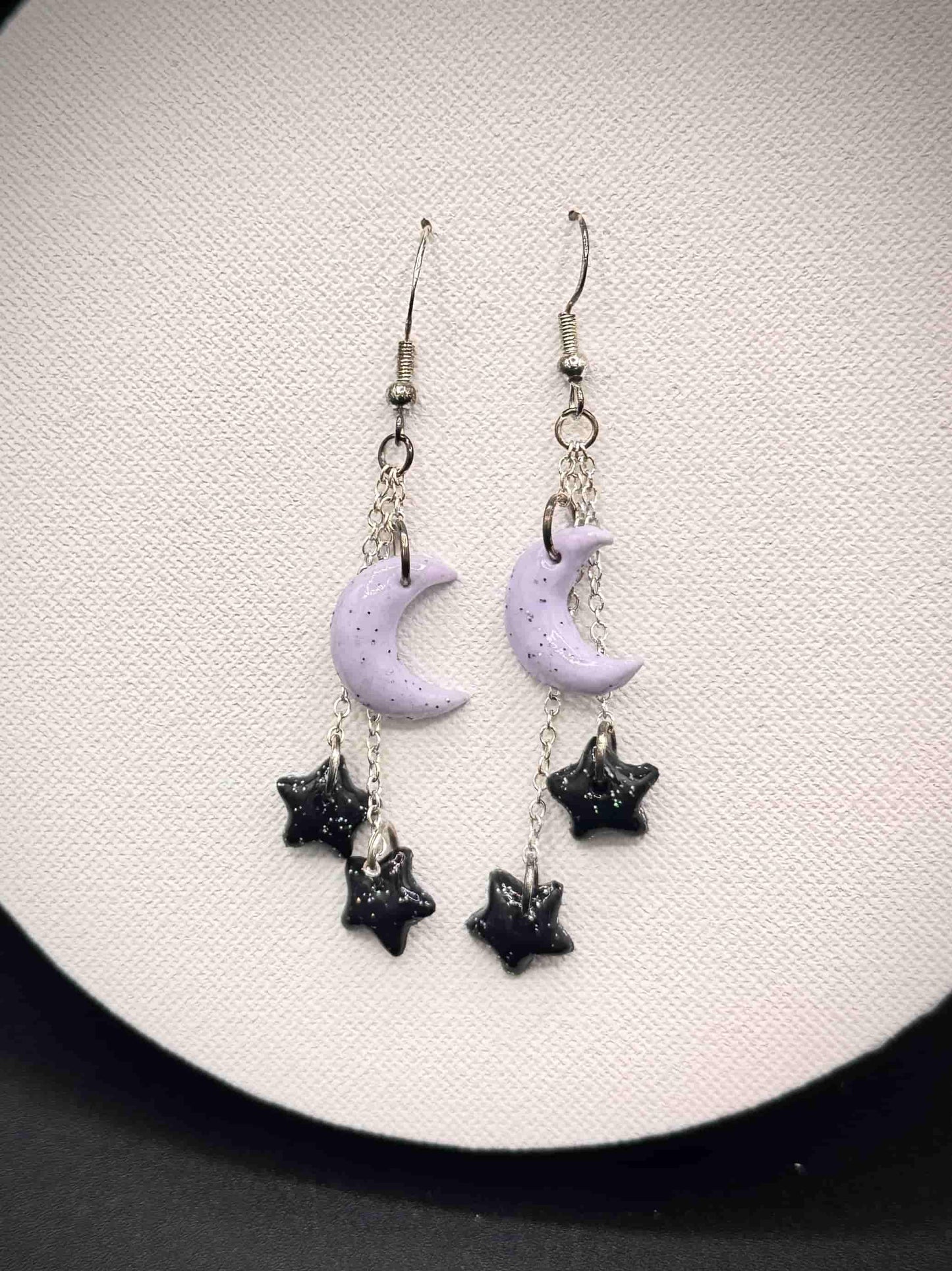 Pair of rainbow glitter purple moon and black star earrings on a white background