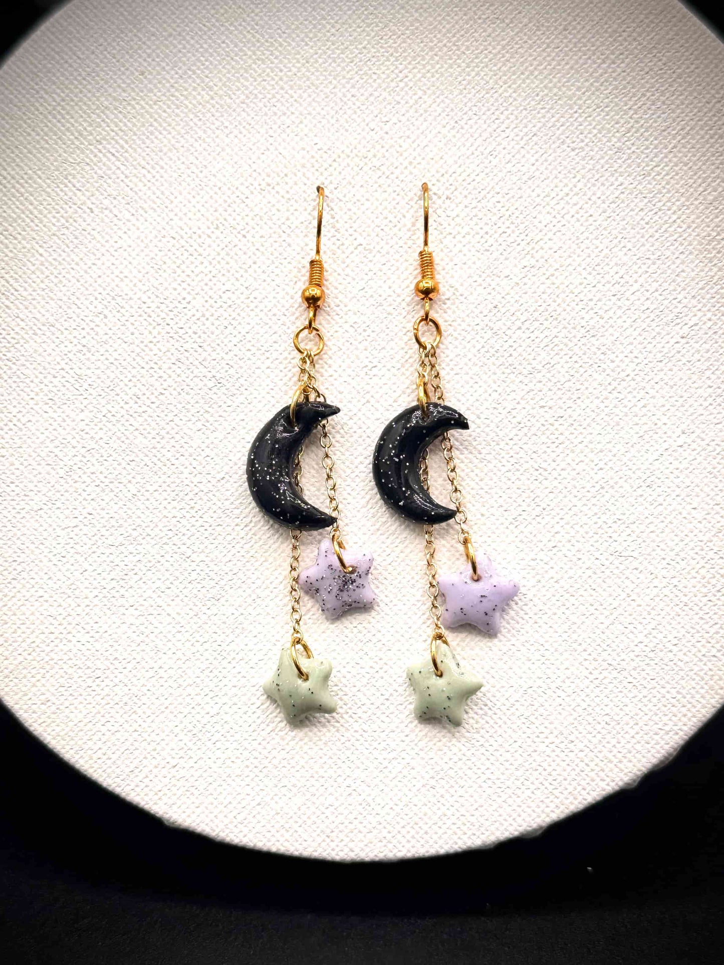 Pair of rainbow glitter black crescent moon and green and purple star earrings with gold hooks on a white background