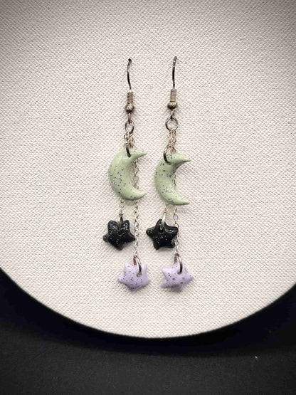 Pair of rainbow glitter green crescent moon and black and purple star earrings on a white background