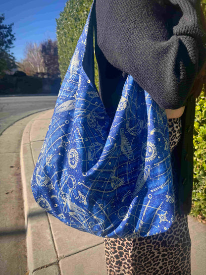 Person holding a blue and white celestial patterned bag outdoors on a sunny day