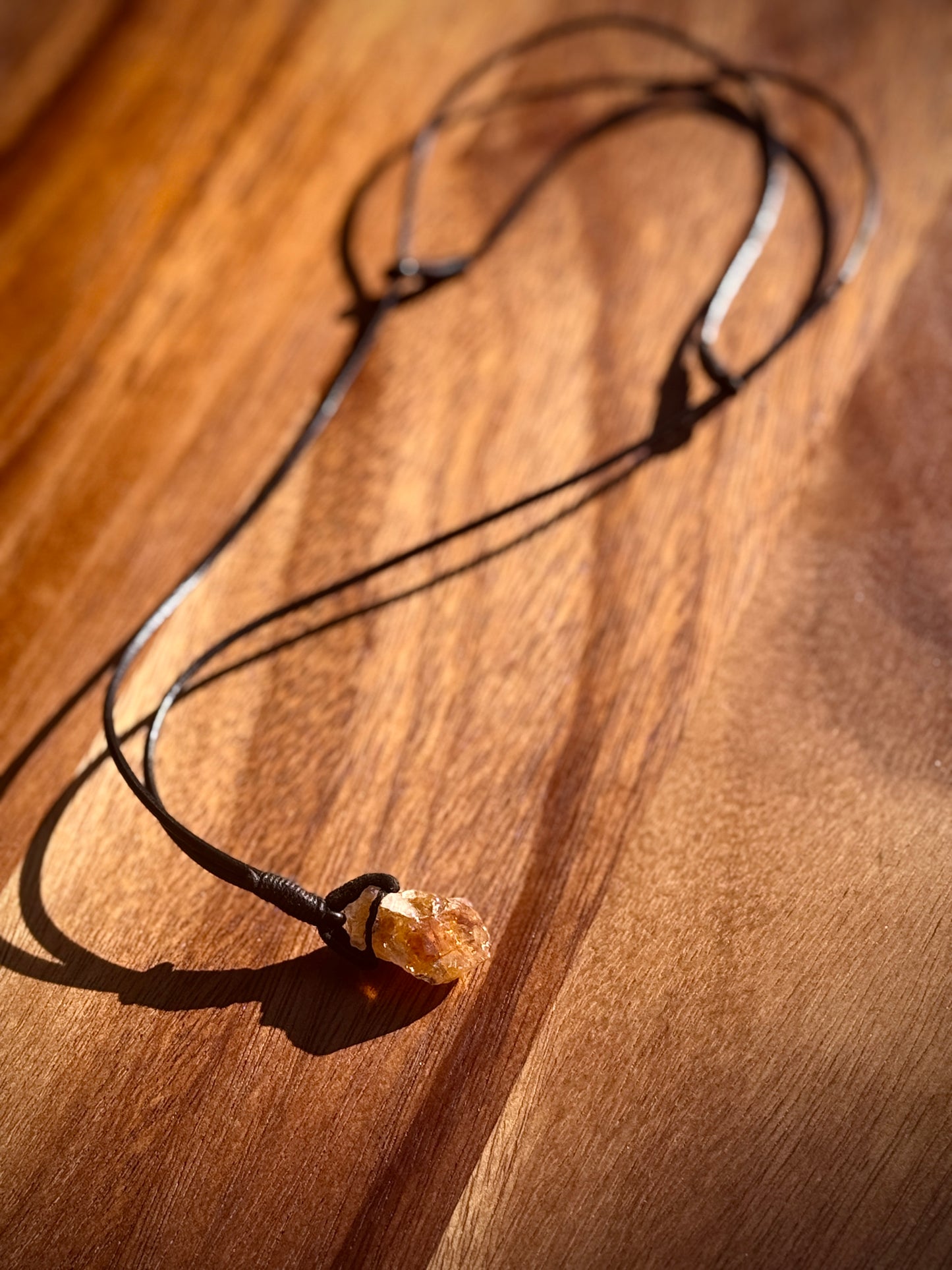 Orange citrine amethyst necklace with leather strap on a wooden table.