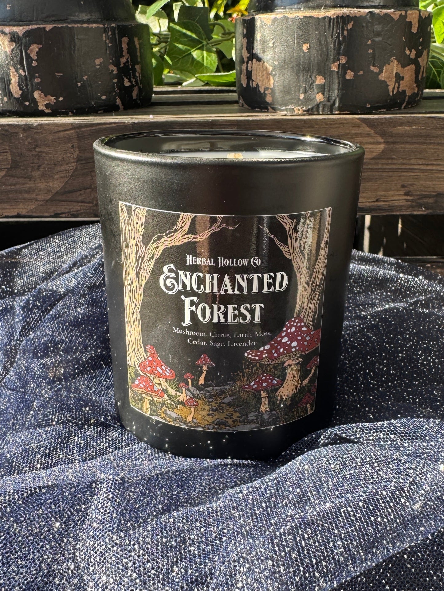 Candle labeled 'Enchanted Forest' on a wooden surface with a textured fabric background.