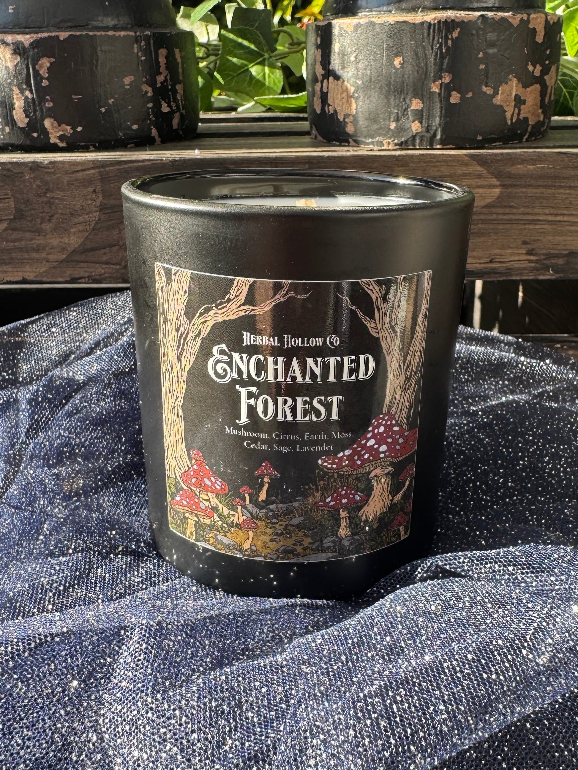 Candle labeled 'Enchanted Forest' on a wooden surface with a textured fabric background.