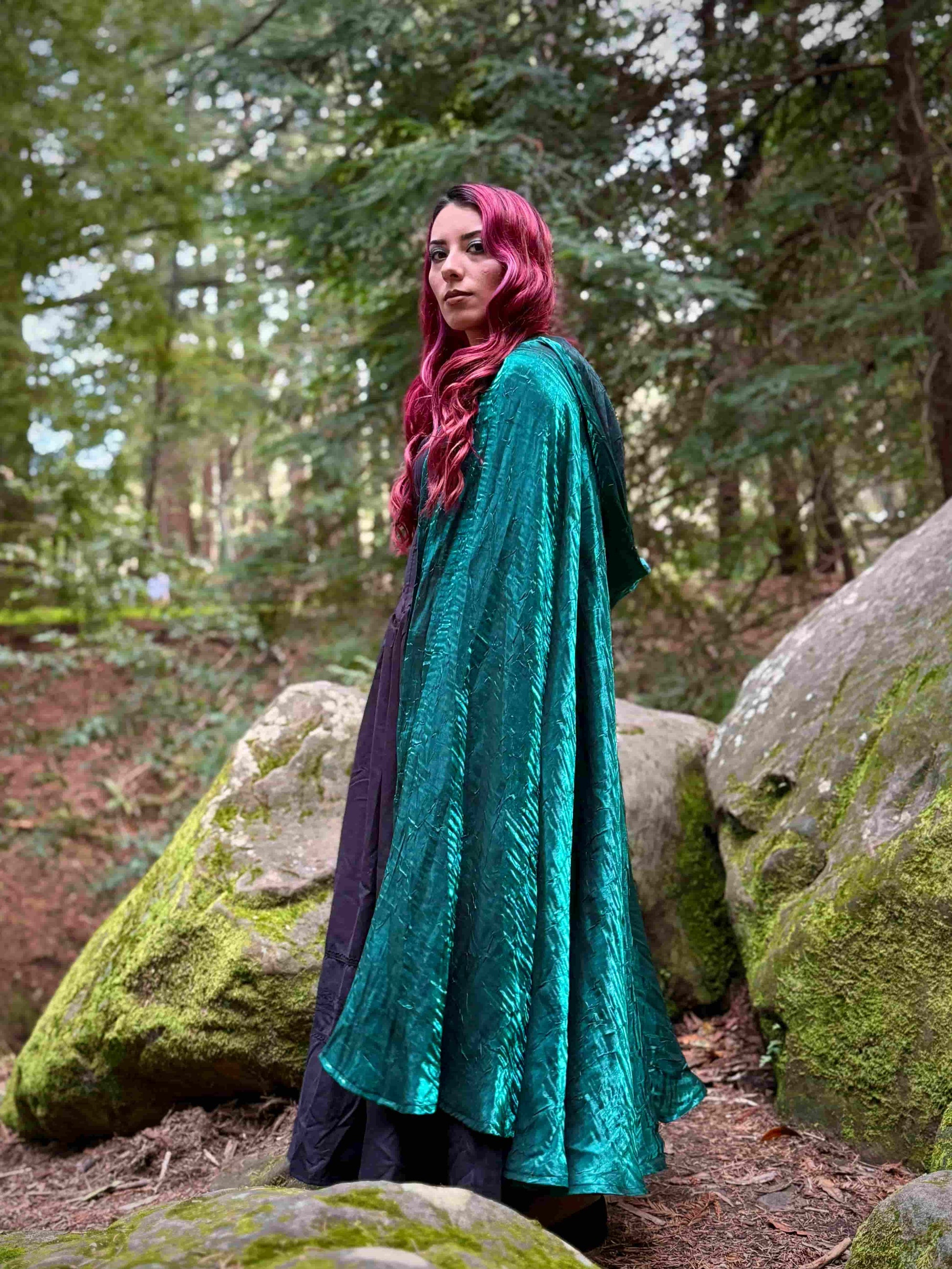 Person wearing a dark teal cloak in a forest setting