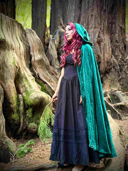 Person with pink hair wearing a green cloak in a forest setting