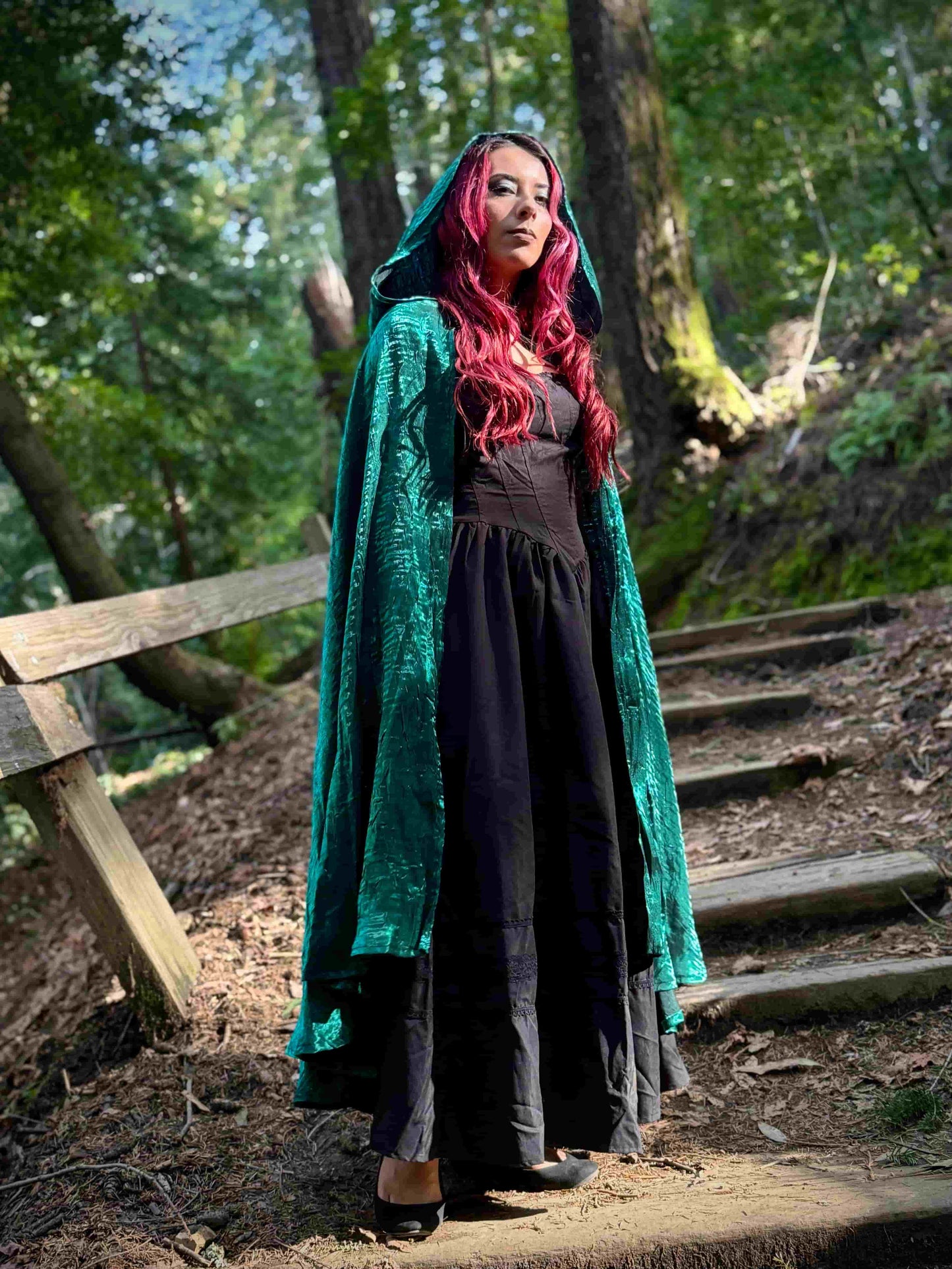 Person with red hair wearing a green cloak in a forest setting