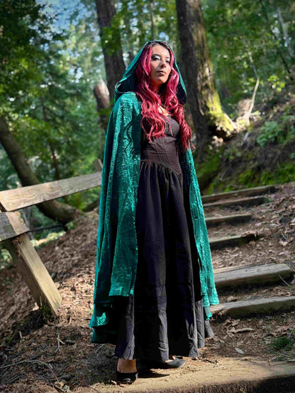 Person with red hair wearing a green cloak in a forest setting