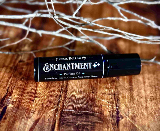 Image of small perfume bottle lying down. Enchantment is a fantasy-inspired rollerball fragrance oil perfume, featuring a handcrafted magical strawberry, black currant, raspberry, and sugar scent.