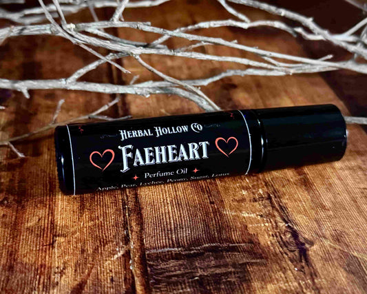 Image of small perfume bottle lying down. Faeheart is a fantasy-inspired rollerball fragrance oil perfume, featuring a handcrafted magical lychee, pear, apple, peony, and lotus flower scent.