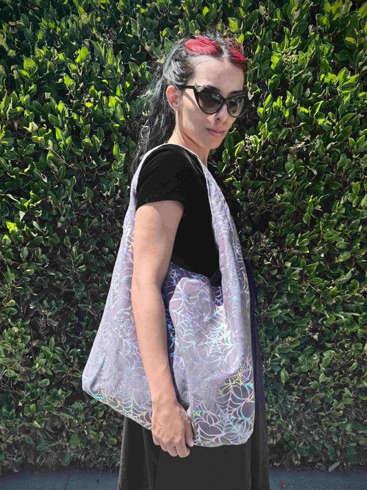 Person wearing a grey and holographic spiderweb bag against a green hedge background