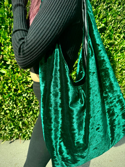 Person holding a green velvet bag against a green hedge background