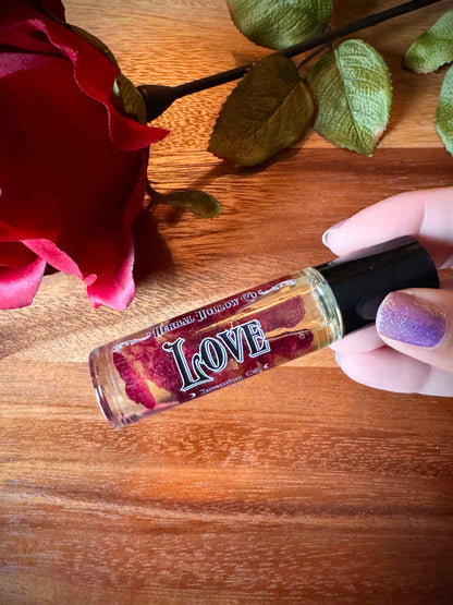 Roll-on oil bottle with rose petals inside labeled 'LOVE' held by a hand with a red rose on a wooden surface