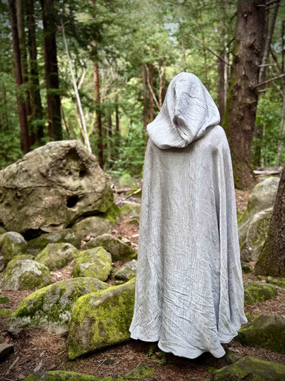 Person in a white hooded cloak standing in a forest setting
