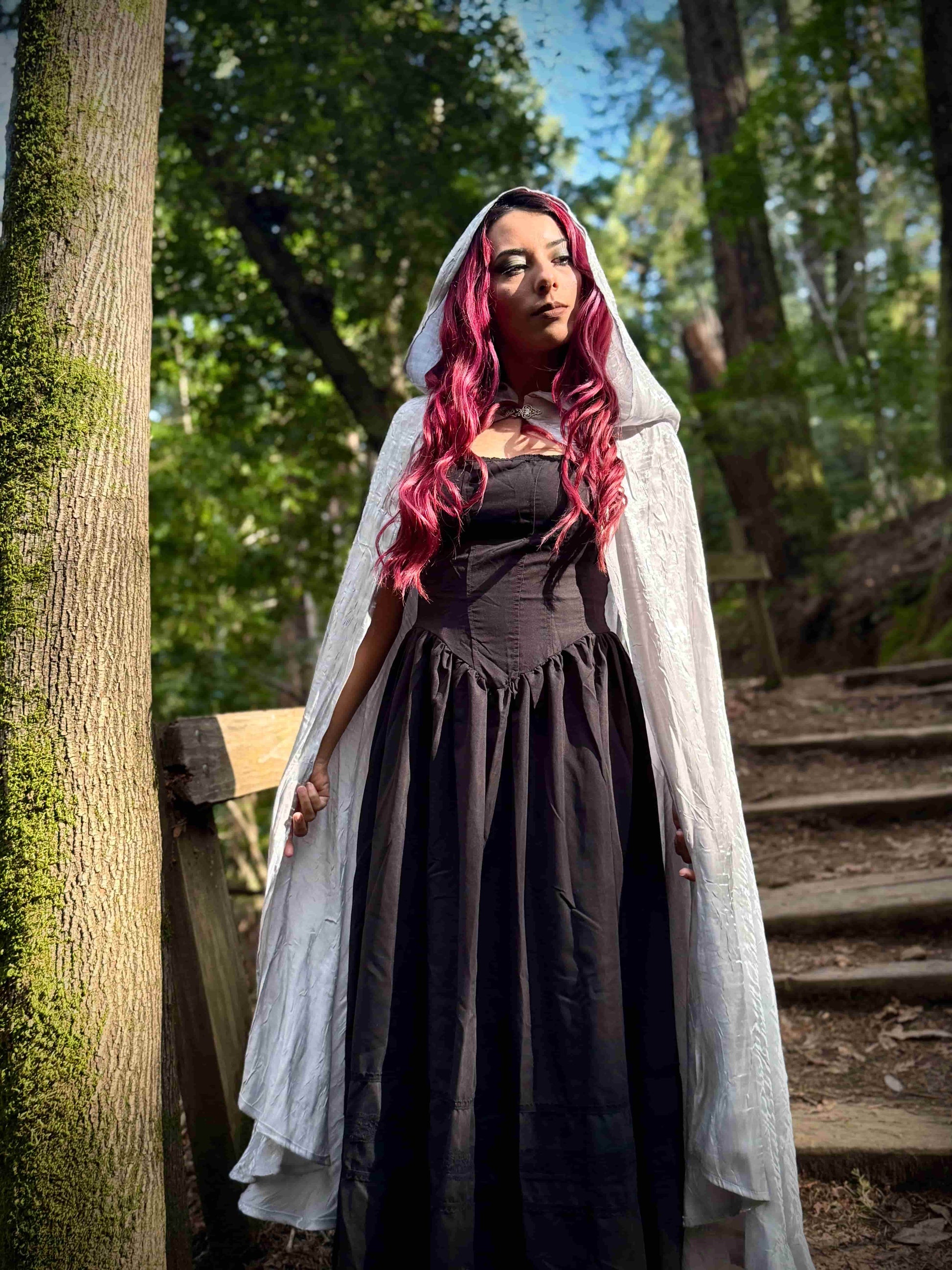 Woman in a white long hooded cloak in a forest setting