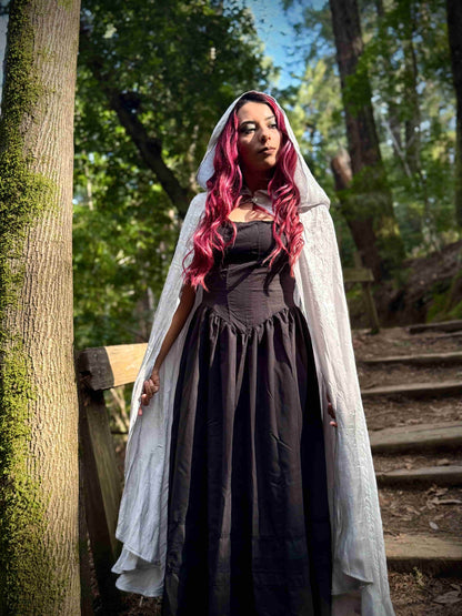 Woman in a white long hooded cloak in a forest setting
