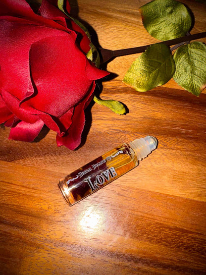 Small bottle labeled 'Love' with rose petals suspended in oil inside of it next to a red rose on a wooden surface