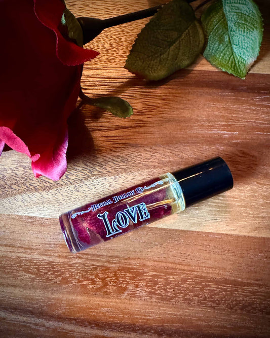 Small bottle labeled 'Love' with rose petals suspended in oil inside of it next to a red rose on a wooden surface