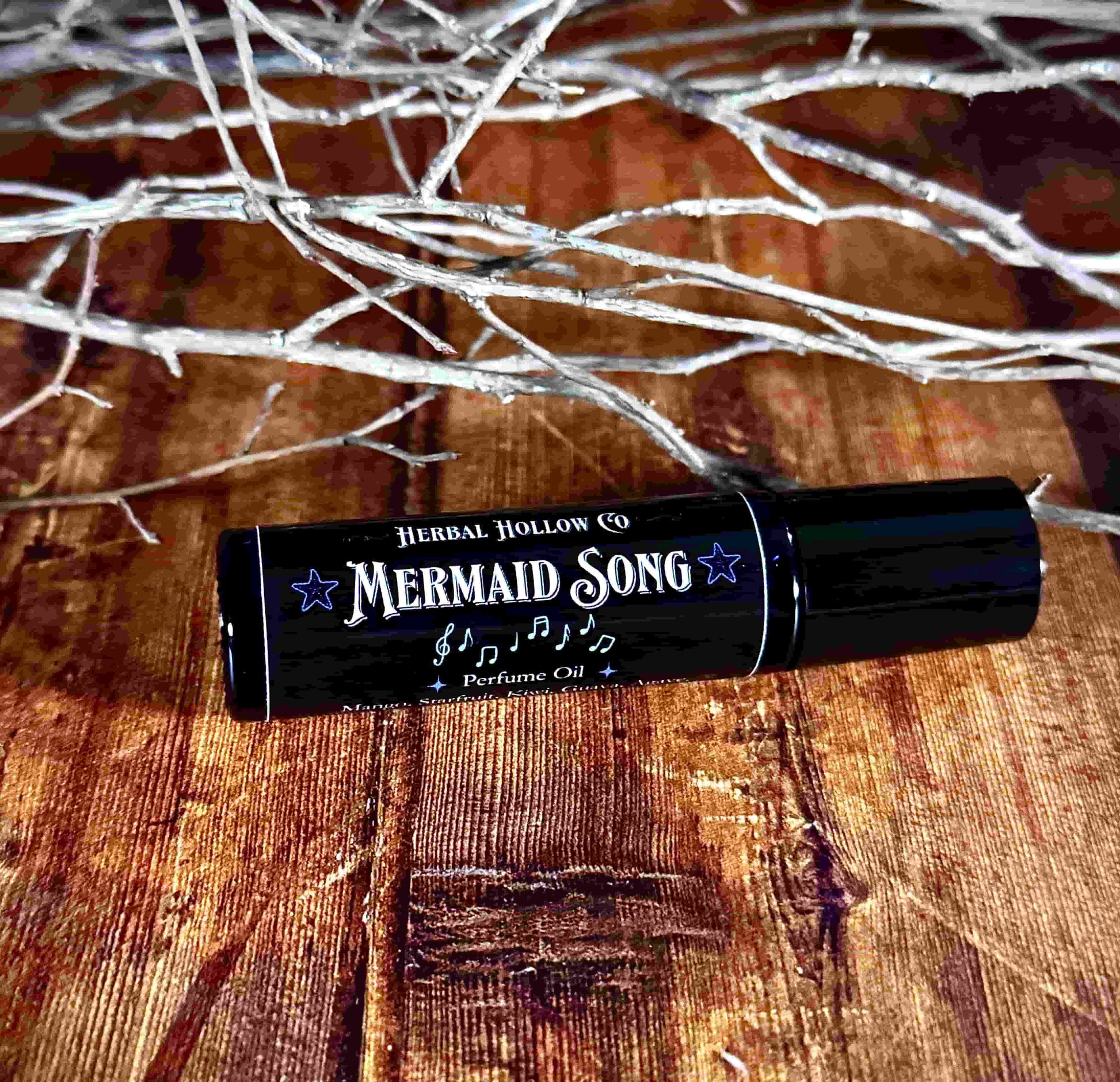Image of small perfume bottle lying down. Mermaid Song is a fantasy-inspired rollerball fragrance oil perfume, featuring a handcrafted magical mango, starfruit, kiwi, agave, and guava scent.