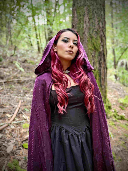 Woman with red hair wearing a purple hooded cloak in a forest setting