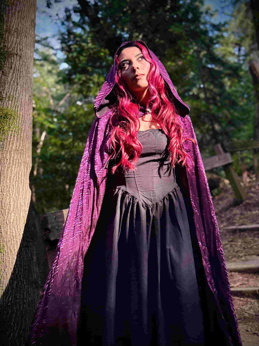 Person with red hair wearing a purple cloak in a forest setting