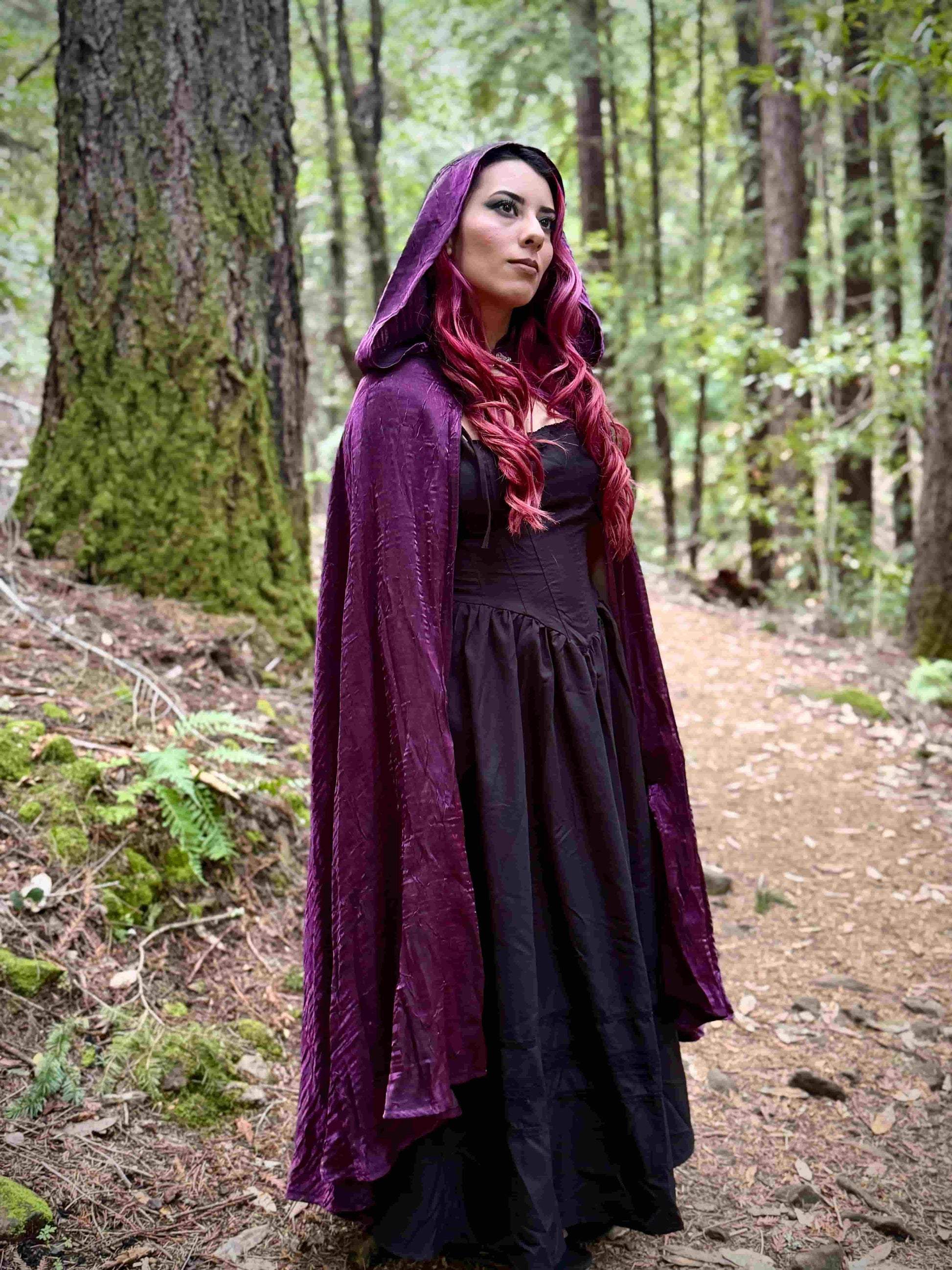 Person wearing a long purple hooded cloak in a forest setting