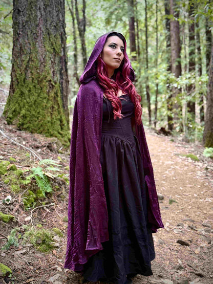Person wearing a long purple hooded cloak in a forest setting