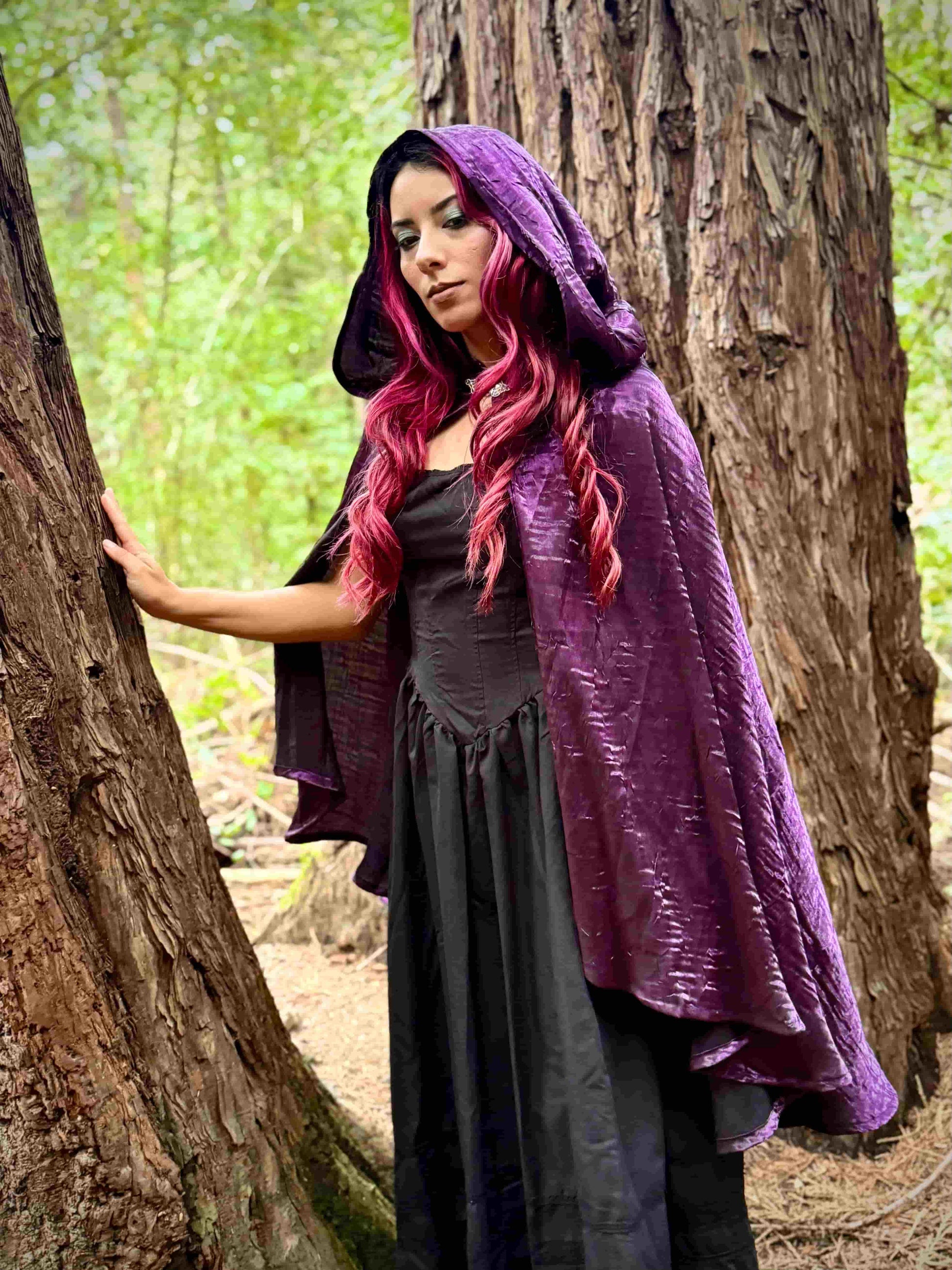 Person wearing a purple hooded cloak in a forest setting