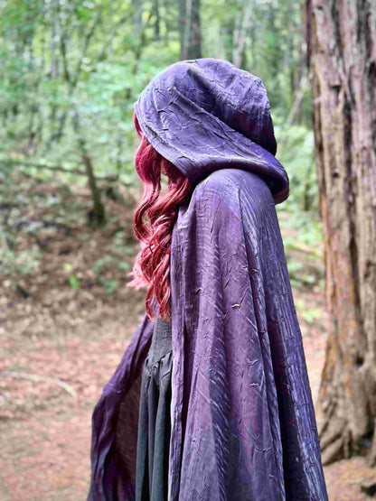 Person wearing a purple cloak with hood in a forest setting