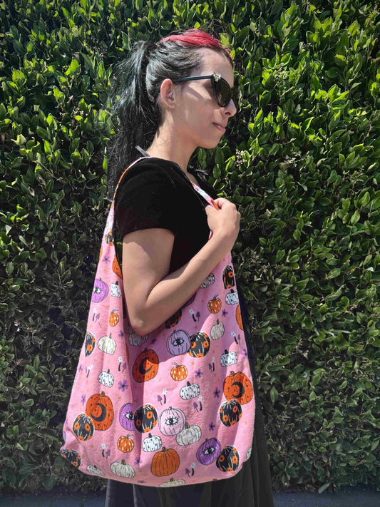 Person wearing a pink bag with Halloween-themed pumpkin designs against a green hedge.