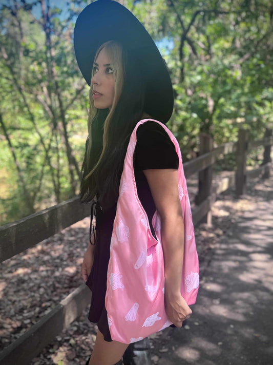 Woman holding a pink shoulder bag with white ghost patterns in a forest setting